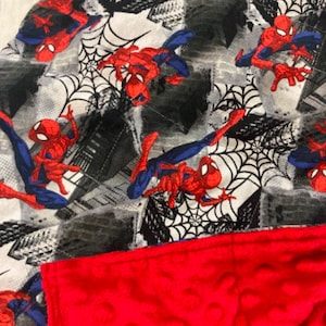 May include: A red and blue Spiderman themed fleece blanket with a red minky backing. The blanket features a repeating pattern of Spiderman characters and webs.