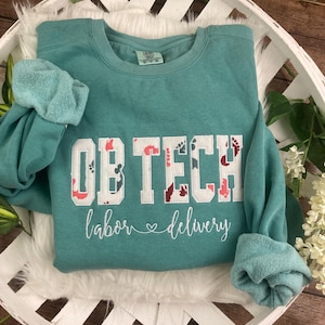 May include: Teal blue sweatshirt with the text "OB TECH labor ♥ delivery" in white with a floral design in red, pink, and blue.
