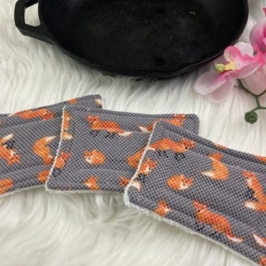 以下が含まれることがあります： オレンジ色のキツネの模様がついた、グレーと白の鍋つかみが3つあります。鍋つかみは柔らかく吸水性のある素材で作られており、熱い鍋やフライパンからカウンタートップを保護するのに最適です。