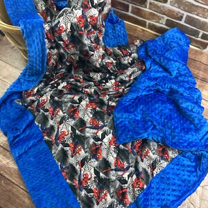 May include: A blue and gray weighted blanket with a Spiderman print. The blanket has a blue minky fabric border and a soft, textured surface.
