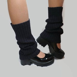 Op de afbeelding: Een paar zwarte gebreide beenwarmers gedragen met zwarte plateau schoenen.