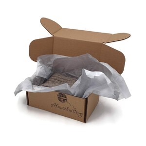 May include: A brown cardboard box with the words "Almazknitting" printed on the front. The box is open and filled with white tissue paper. A brown and white striped fabric is visible inside the box.