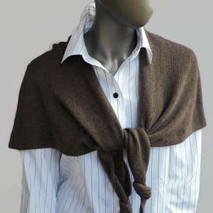 Puede incluir: Una bufanda de punto marrón atada alrededor del cuello de una camisa blanca con cuello y rayas verticales.