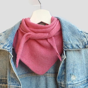 Puede incluir: Una bufanda de punto rosa con un borde deshilachado, drapeada sobre una chaqueta vaquera azul claro.