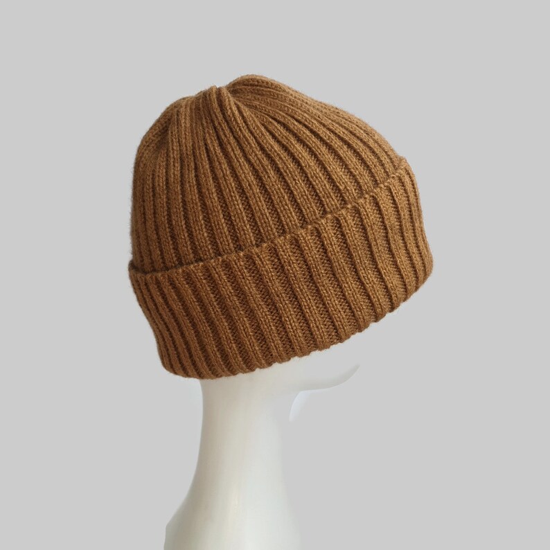 May include: A brown ribbed knit beanie hat. The hat is folded down at the brim and is made of a soft, warm material.