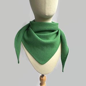 May include: A solid green triangular scarf featuring a fine knit texture. The scarf is draped around a mannequin neck, displaying a pointed front edge and two side ends that hang down, showcasing a consistent grass green color throughout.