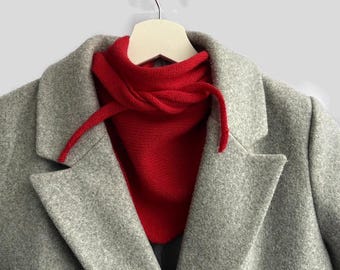 May include: A gray wool coat with a red knit scarf tied around the neck.