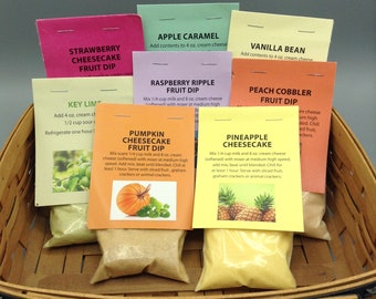 May include: A basket filled with small bags of fruit dip mix. The bags are labeled with different flavors, including Strawberry Cheesecake, Key Lime, Raspberry Ripple, Apple Caramel, Pumpkin Cheesecake, Pineapple Cheesecake, Peach Cobbler, and Vanilla Bean. Each bag includes instructions for mixing the dip with cream cheese and milk.