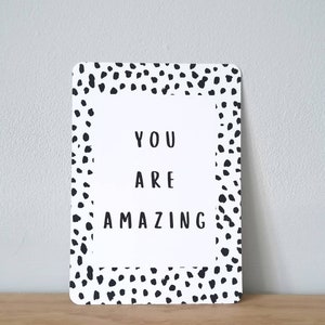 Op de afbeelding: Een witte kaart met zwarte stippen rond de rand. De kaart zegt "You are amazing" in zwarte tekst.