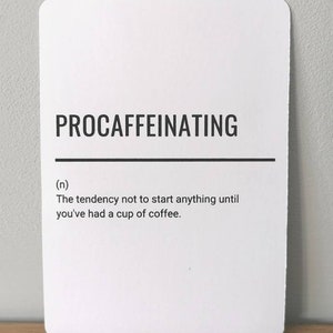 Op de afbeelding: Een witte kaart met zwarte tekst die "procaffeinating" definieert als de neiging om niets te beginnen voordat je een kop koffie hebt gedronken.