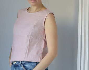 May include: A woman wearing a pink sleeveless top and blue jeans. She has her hair pulled back in a bun with a yellow scrunchie.