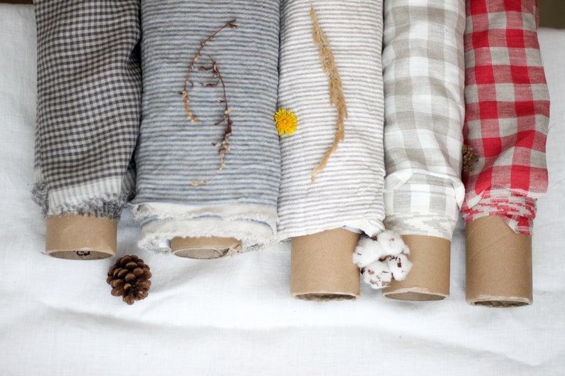 May include: Five rolls of fabric in different patterns and colors. The fabrics are rolled up and tied with twine. The fabrics are a gingham pattern in black and white, a striped pattern in blue and white, a striped pattern in gray and white, a gingham pattern in white and beige, and a gingham pattern in red and white.