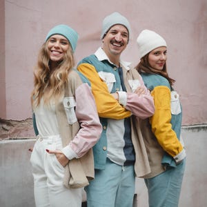 May include: Three people wearing colorful corduroy jackets and beanies. The jackets are made of different colors of corduroy, including pink, blue, yellow, and beige. The beanies are in shades of blue and white.