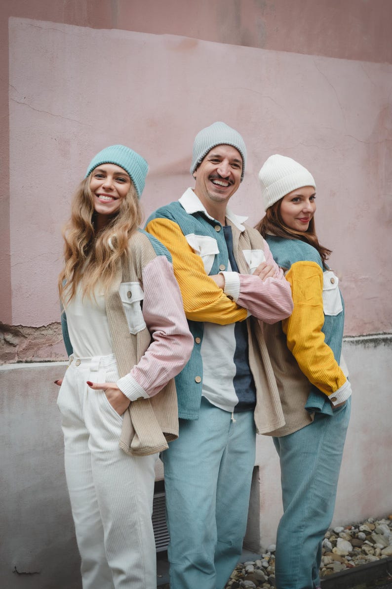 May include: Three people wearing colorful corduroy jackets and beanies. The jackets are made of different colors of corduroy, including pink, blue, yellow, and beige. The beanies are in shades of blue and white.