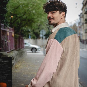 May include: A person wearing a multi-colored corduroy shirt with a pink, beige, and green color scheme. The shirt has a collar and long sleeves.