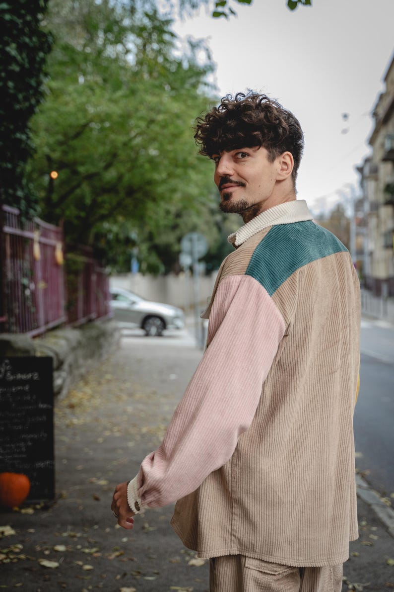 May include: A person wearing a multi-colored corduroy shirt with a pink, beige, and green color scheme. The shirt has a collar and long sleeves.