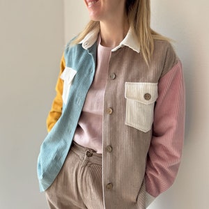 May include: A brown corduroy shirt with a blue, white, and yellow patchwork design. The shirt has a white collar and a button-up front.