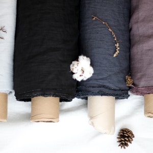 May include: Four rolls of fabric in different colors: light gray, black, dark gray, and mauve. The fabric is rolled up and tied with a brown ribbon. The fabric is on a white surface.