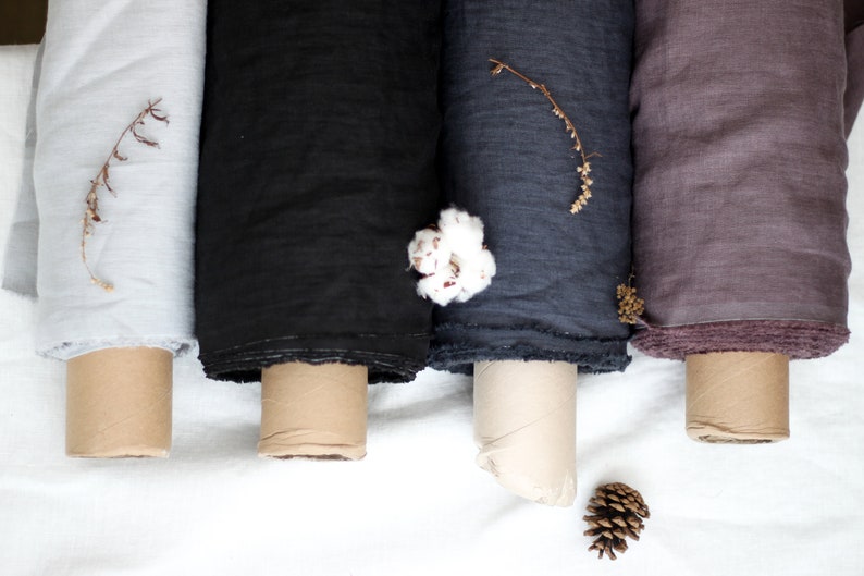 May include: Four rolls of fabric in different colors: light gray, black, dark gray, and mauve. The fabric is rolled up and tied with a brown ribbon. The fabric is on a white surface.