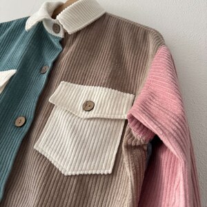 May include: A corduroy shirt with a brown, pink, and teal color block design. The shirt has a button-up front and two pockets.