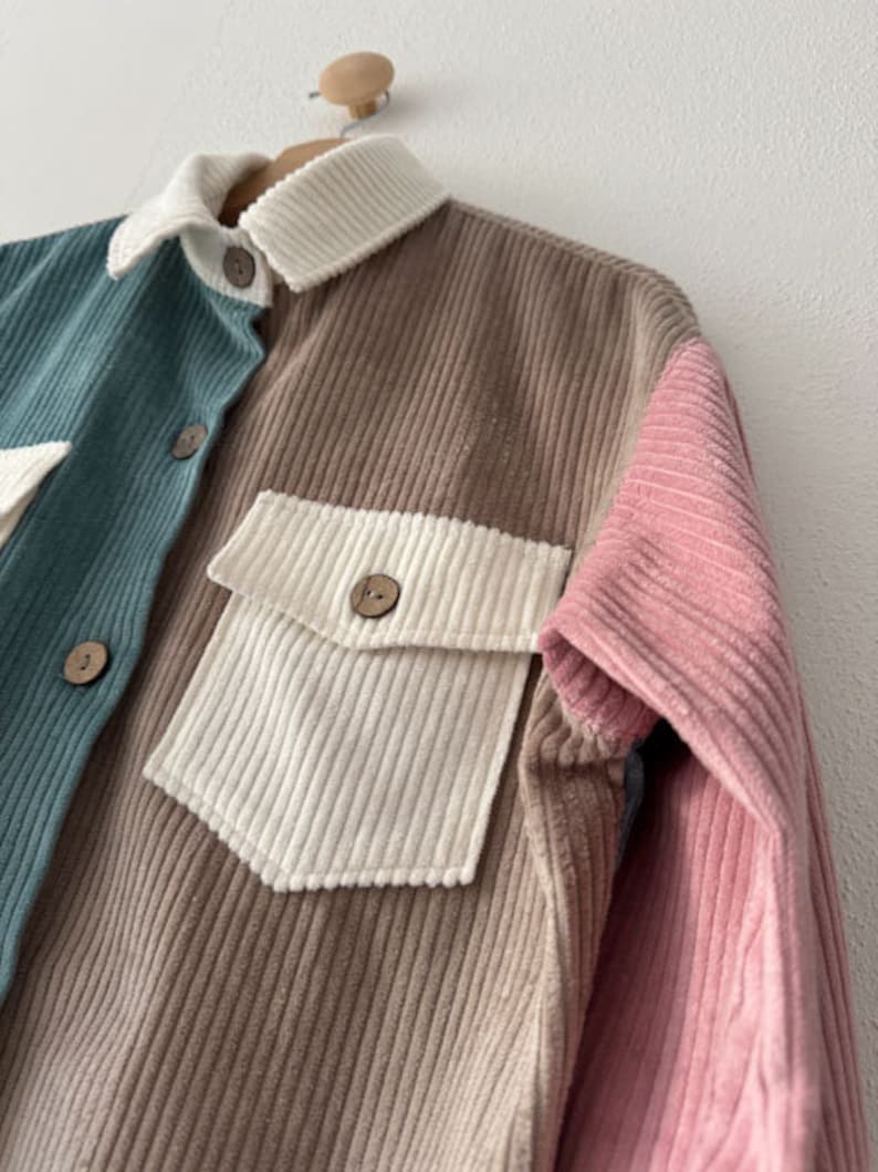 May include: A corduroy shirt with a brown, pink, and teal color block design. The shirt has a button-up front and two pockets.