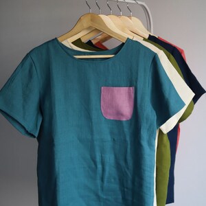 Pu&ograve; includere: Una t-shirt in lino turchese a maniche corte con una tasca a toppa rosa.