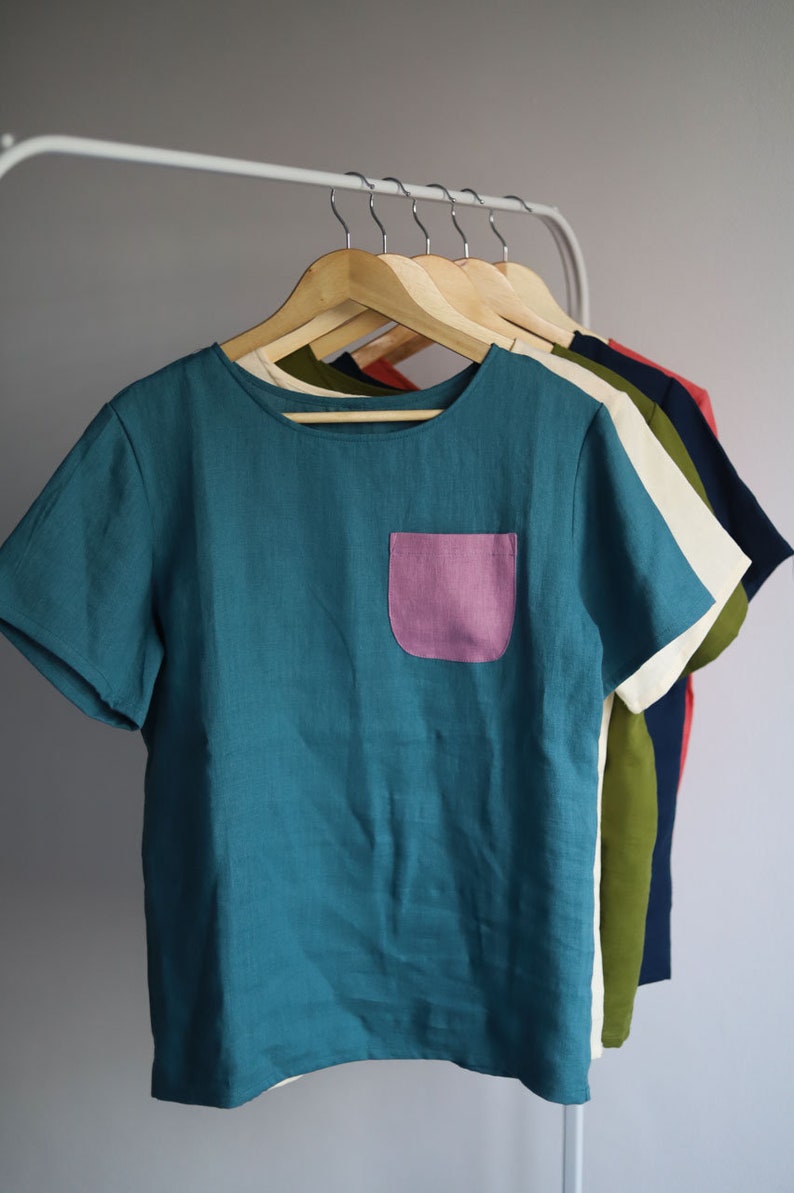 Pu&ograve; includere: Una t-shirt in lino turchese a maniche corte con una tasca a toppa rosa.
