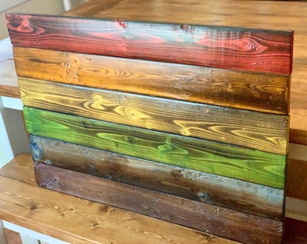 May include: A wooden wall art piece with a rainbow design. The wood is stained in different colors, including red, orange, yellow, green, blue, and brown. The wood is arranged in horizontal stripes.