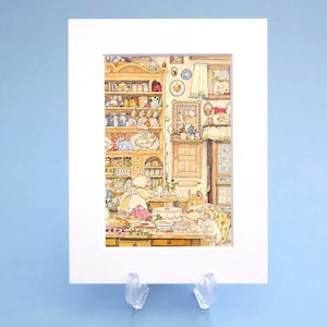 May include: A matted art print featuring a detailed watercolour illustration of two anthropomorphic mice baking in a rustic kitchen. The scene includes a wooden hutch filled with dishes, a window with curtains, and a table covered with various baked goods.