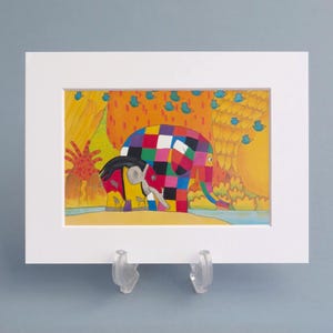 May include: A matted art print featuring a colourful patchwork elephant with a grid of red, blue, yellow, green, and black squares. A smaller grey elephant stands beside it near a blue river, with orange trees and blue birds in the background.