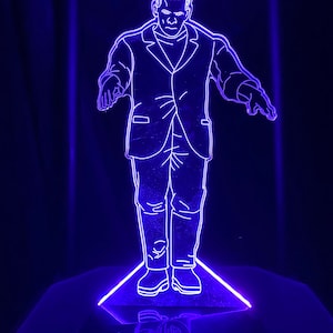May include: A blue neon light sculpture of a person in a suit standing with arms outstretched. The sculpture is on a triangular base.