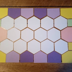 May include: A set of colourful paper shapes, including hexagons, squares, and pentagons, arranged in a honeycomb pattern. The shapes are in shades of yellow, green, pink, and purple.