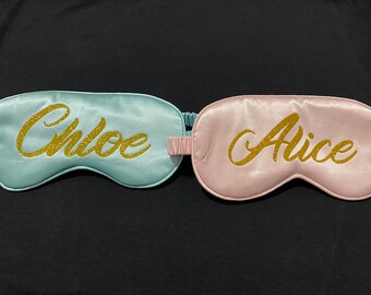 May include: Two satin sleep masks, one light blue with the name "Chloe" in gold glitter lettering and one pink with the name "Alice" in gold glitter lettering.