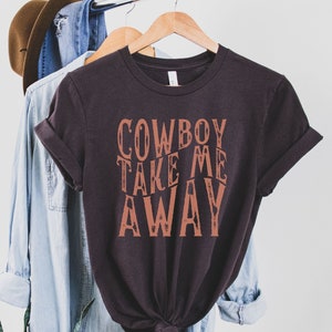 May include: A dark brown t-shirt with the text "COWBOY TAKE ME AWAY" printed in a distressed orange font.