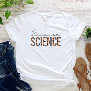 May include: White t-shirt with the text "Because Science" printed in black with a leopard print design behind the word "Science".