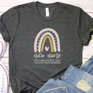 May include: A dark gray t-shirt with a rainbow design and the text "NICU NURSE IT'S A BEAUTIFUL DAY TO SAVE TINY HUMANS".