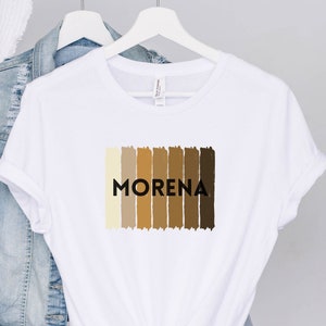 May include: White t-shirt with a graphic of a spectrum of brown skin tones and the word "MORENA" in black text.