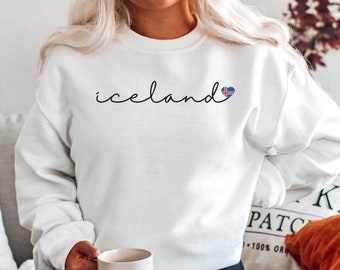 May include: White sweatshirt with the word "iceland" written in black cursive script and a small heart with the Icelandic flag inside.