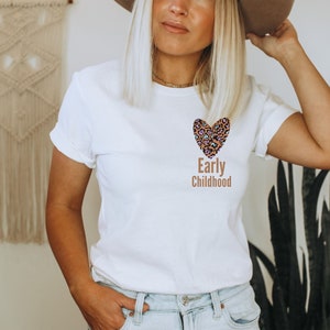 May include: White t-shirt with a brown leopard print heart and the text "Early Childhood" printed on the front.