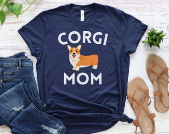 May include: A navy blue t-shirt with white text that reads "Corgi Mom". A cartoon image of a corgi dog is above the text.