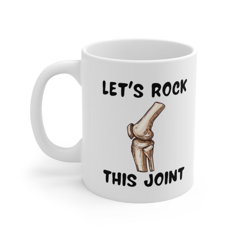 May include: White ceramic coffee mug with a black illustration of a knee bone and the text "Let's Rock This Joint".