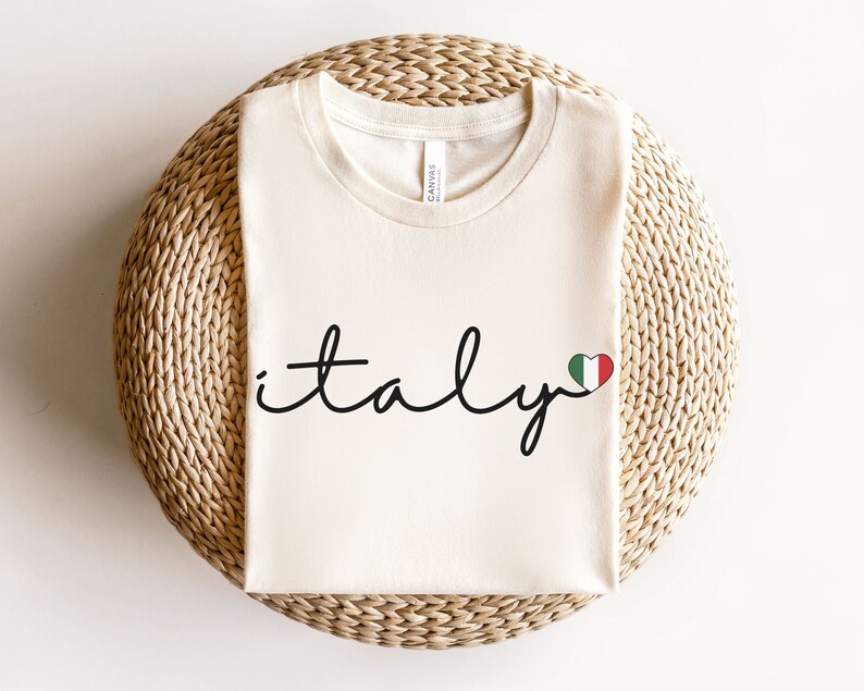 May include: A white t-shirt with the word "italy" written in black cursive script with a small red, white, and green heart with the Italian flag colors next to it.