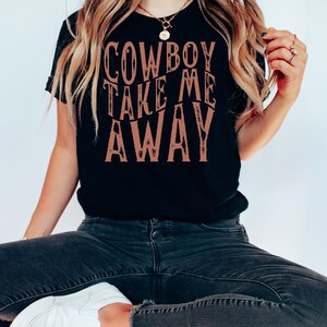May include: A black t-shirt with the text "COWBOY TAKE ME AWAY" printed in brown on the front.