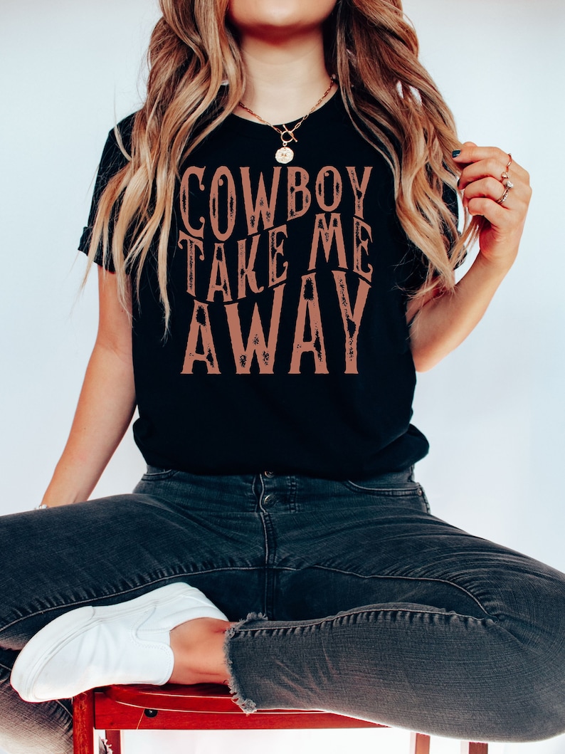 May include: A black t-shirt with the text "COWBOY TAKE ME AWAY" printed in brown on the front.
