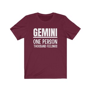 May include: A maroon t-shirt with white text that reads "GEMINI ONE PERSON THOUSAND FEELINGS".
