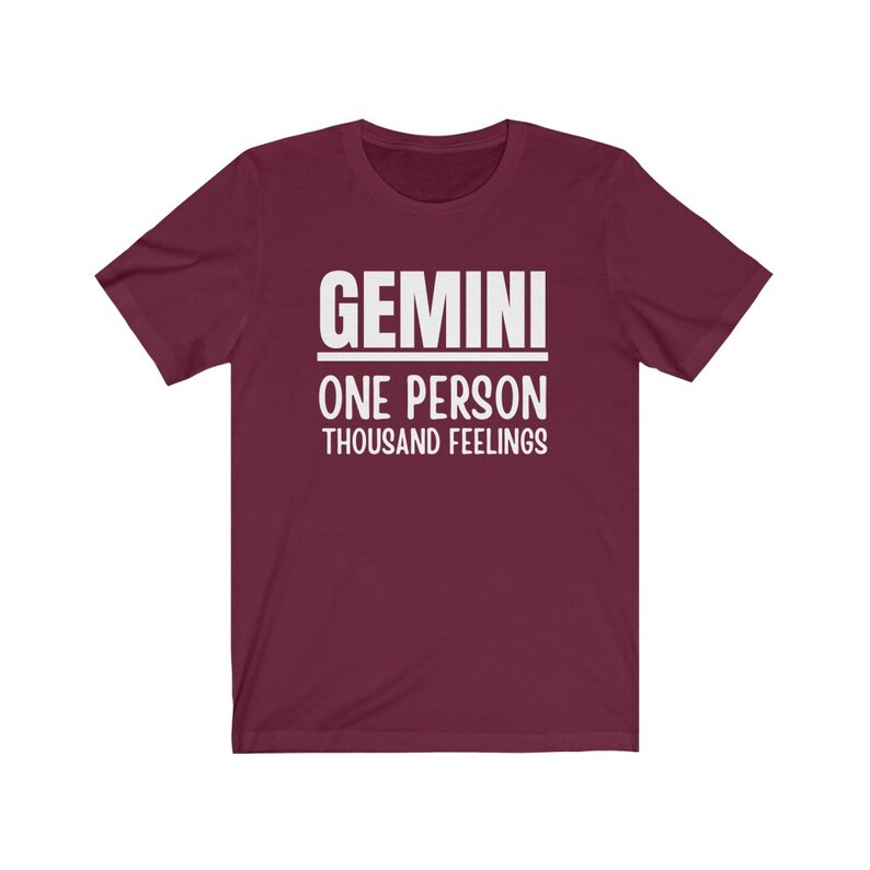 May include: A maroon t-shirt with white text that reads "GEMINI ONE PERSON THOUSAND FEELINGS".
