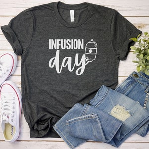 May include: A dark gray t-shirt with the text "INFUSION day" in white lettering. A small white graphic of an IV bag with a cross is next to the text.