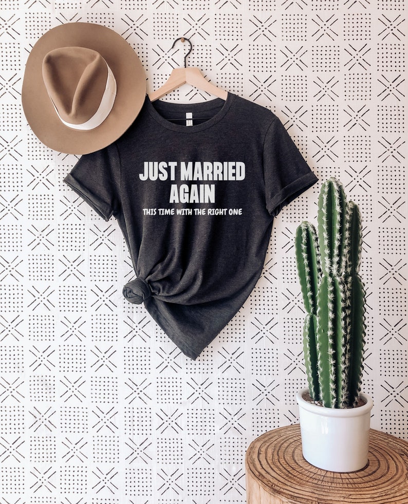 May include: A dark grey t-shirt with the text "Just Married Again This Time With The Right One" in white lettering.