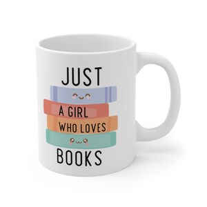 Op de afbeelding: Witte keramische mok met de tekst "JUST A GIRL WHO LOVES BOOKS" in zwart. De tekst staat op een stapel kleurrijke boeken met cartoonogen.