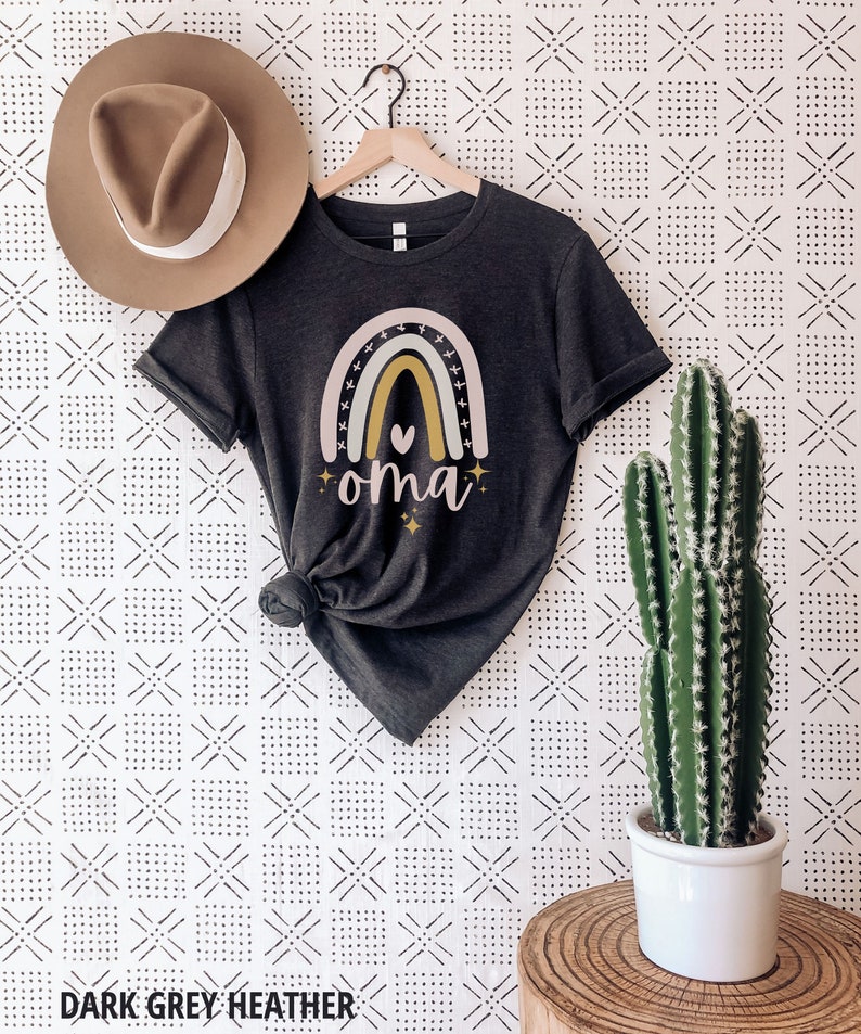 May include: A dark grey heather t-shirt with a rainbow design and the word "oma" in gold lettering. The rainbow has a pink, yellow, and green color scheme with a small heart in the center.